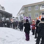 Des manifestants se tiennent dehors devant un édifice en hiver.